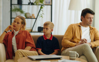 A mother and father sit on either side of their child looking away from each other.