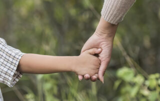 A closeup image of a child’s hand being held by a parent’s hand.