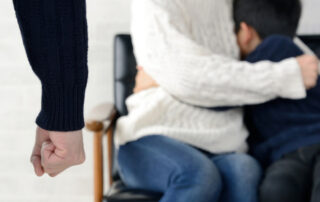 A man with enclosed fist stands in front of a woman and child who cower.