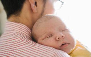 A man holds an infant child who rests against his shoulder.