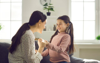A mother and child smile while holding hands on the couch in a living room.